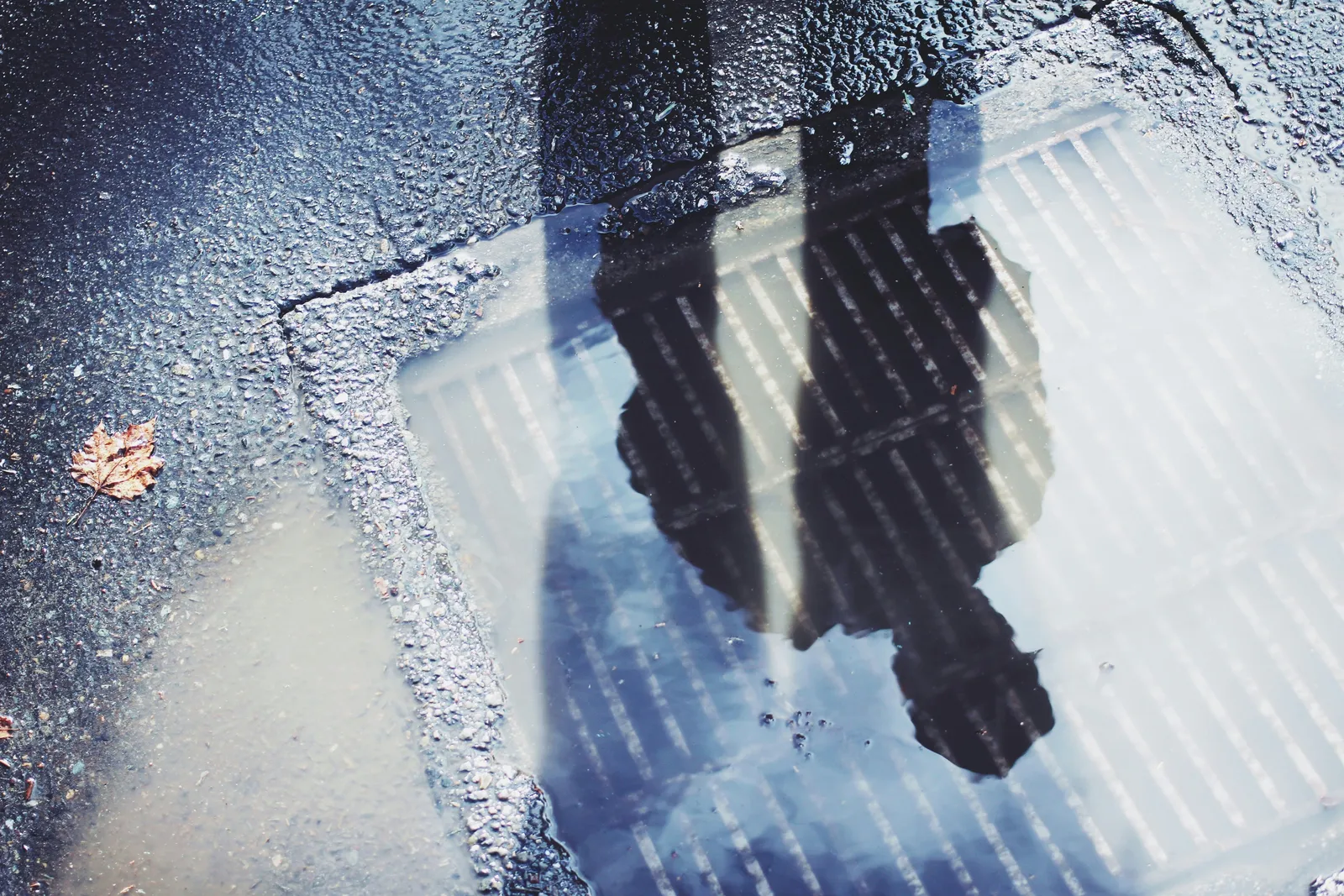 FixMyStreet: 6 months in A person's reflection in a rain puddle over a drain grate on a cracked, wet road