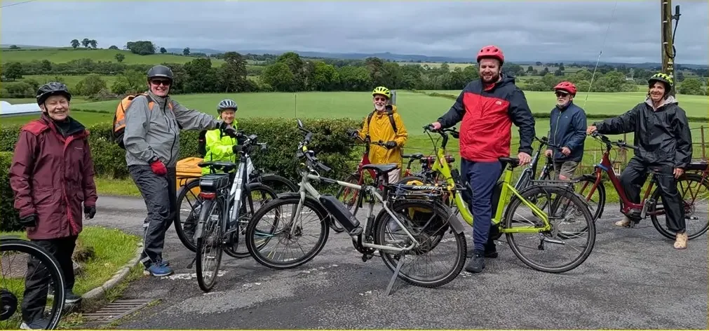 Eight riders in waterproofs and helmets standing with their e-bikes on a country road outside Dumfries
